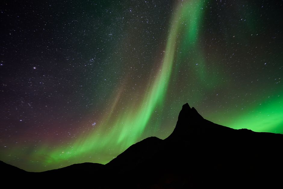Green aurora glowing above a dark mountain ridge under a star-filled night sky.