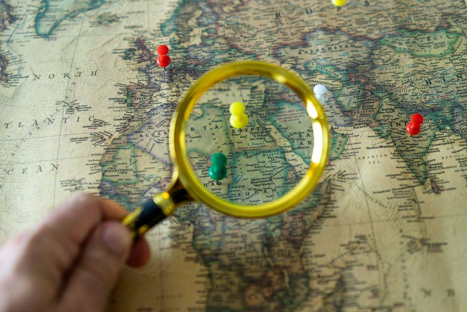 Vintage paper map marked with colored pins and viewed through a handheld magnifying glass.