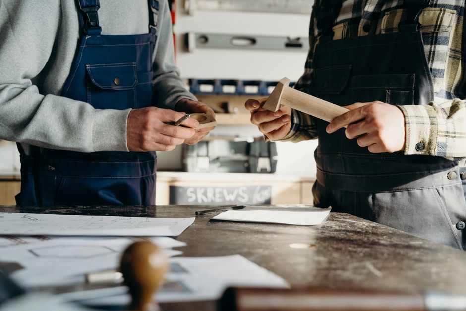 Two makers comparing plans and small materials across a busy workshop table.
